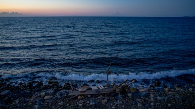 Ocean waves gently lap a rocky shore at dusk.